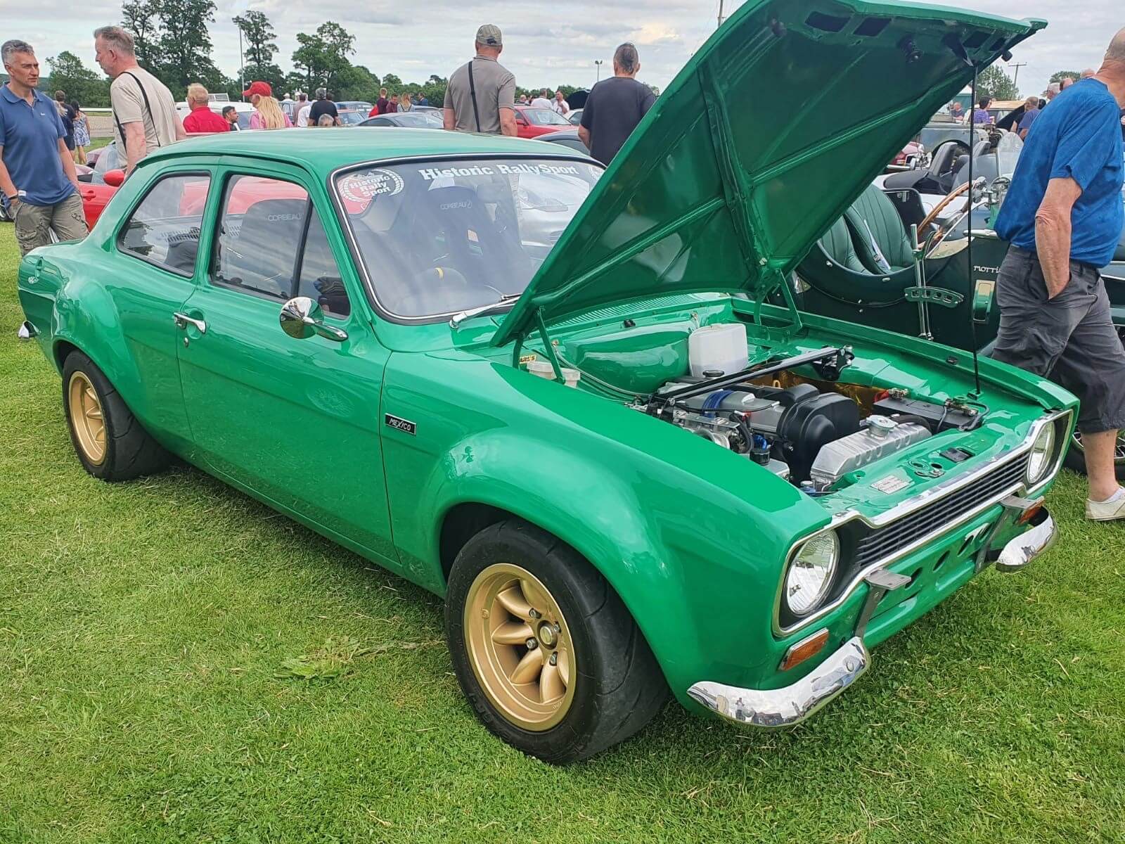 Green Ford Escort Mk1 with gold alloys displayed at a classic car show