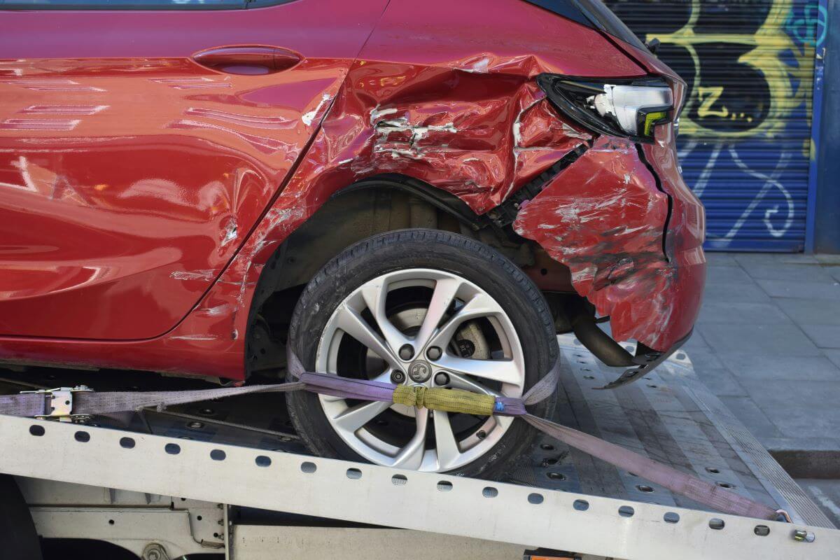 Red Vauxhall with dented rear wheel arch being towed